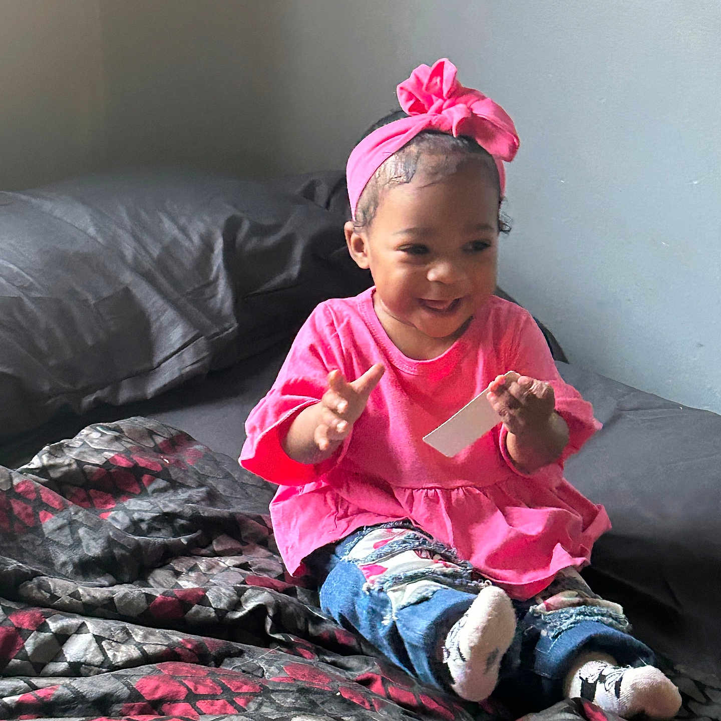 Zyura is registered to the contest to win money with this photo: bed, blanket, casual_clothing, child, clapping, cute, happy, headband, home, indoors, patterned_blanket, person, pink_clothing, playful, portrait, seated, smiling, socks, toddler, young_child
