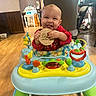 baby, child, walker, toy, indoor, floor, wooden_sign, red_clothing, smiling, tongue_out, happy, playful, colorful, furniture, home, flooring, person, infant, cute, baby_toy