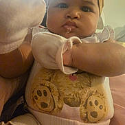 Tia is registered to the contest to win money with this photo: baby, infant, close_up, face, headband, onesie, teddy_bear_print, drool, hand, mitten, curious_expression, indoor, portrait, child, cute, soft_lighting, skin, person, clothing, young_child