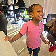 Talea is registered to the contest to win money with this photo: child, girl, smiling, pink_shirt, jeans, sneakers, indoor, table, chair, person, happy, hair_ties, dreadlocks, casual, footwear, young_adult, hoodie, seated, daylight, floor