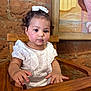 baby, child, girl, white_dress, bow, high_chair, wooden_chair, curly_hair, indoors, brick_wall, painting, cute, portrait, sitting, hand, face, expression, skin, furniture, young