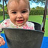 toddler, child, swing, playground, smiling, happy, outdoor, greenery, blue_surface, flower_print, hair_clip, face, eyes, cute, joyful, baby, play, seat, metal_chains, nature