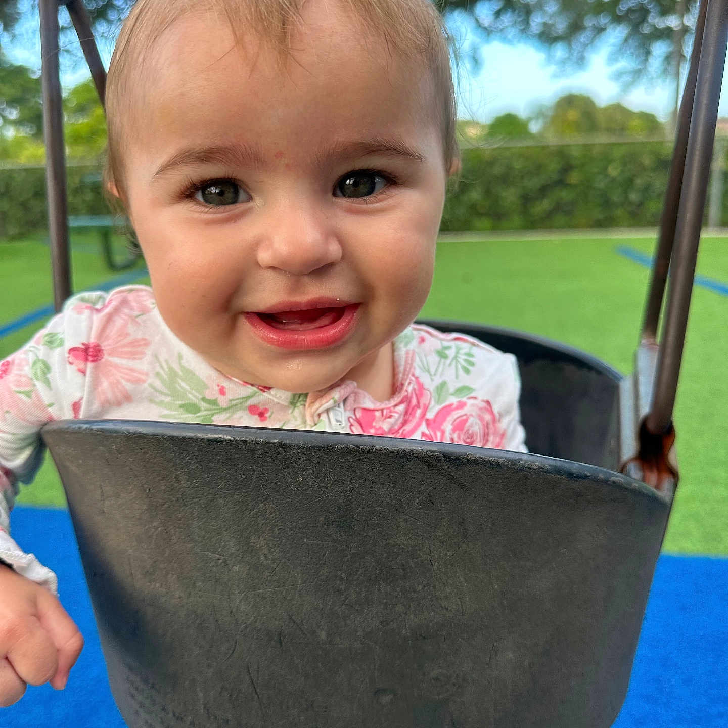 Lia joined the competition — help win amazing prizes! toddler, child, swing, playground, smiling, happy, outdoor, greenery, blue_surface, flower_print, hair_clip, face, eyes, cute, joyful, baby, play, seat, metal_chains, nature