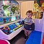 child, toddler, arcade, ride, buttons, map, world_map, curly_hair, sweater, pants, shoes, indoor, lights, festive, playful, colorful, interactive, entertainment, shopping_mall, curiosity