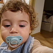 Gonçalo a rejoint le concours — aidez-le/la à gagner de superbes lots ! toddler, child, pacifier, curly_hair, indoor, baby_bib, face, young_child, person, home, wooden_floor, blanket, sleepwear, light_skin, cute, portrait, closeup, infant, expressionless, baby_clothing