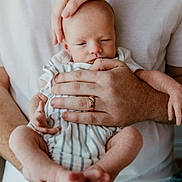 Kashton Smith is registered to the contest to win money with this photo: baby, infant, newborn, hands, striped_clothing, white_shirt, adult, cradling, close_up, skin, peaceful, sleepy, parent, family, caring, tenderness, human, portrait, indoor, love