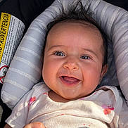 Berkeh is registered to the contest to win money with this photo: baby, infant, smiling, car_seat, onesie, hair, face, eyes, mouth, hand, closeup, portrait, cushion, seat, sunlight, shadow, label, sticker, happy, rosy_cheeks