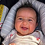 baby, infant, smiling, car_seat, onesie, hair, face, eyes, mouth, hand, closeup, portrait, cushion, seat, sunlight, shadow, label, sticker, happy, rosy_cheeks