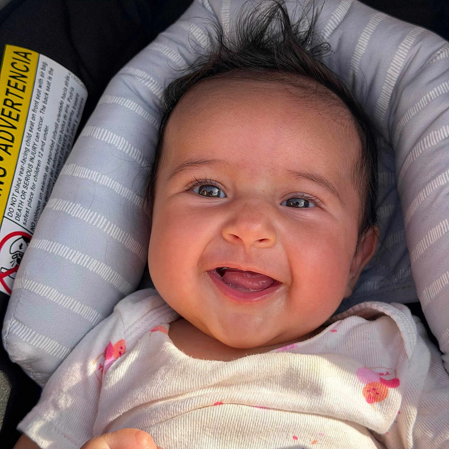 Berkeh is registered to the contest to win money with this photo: baby, car_seat, closeup, cushion, eyes, face, hair, hand, happy, infant, label, mouth, onesie, portrait, rosy_cheeks, seat, shadow, smiling, sticker, sunlight