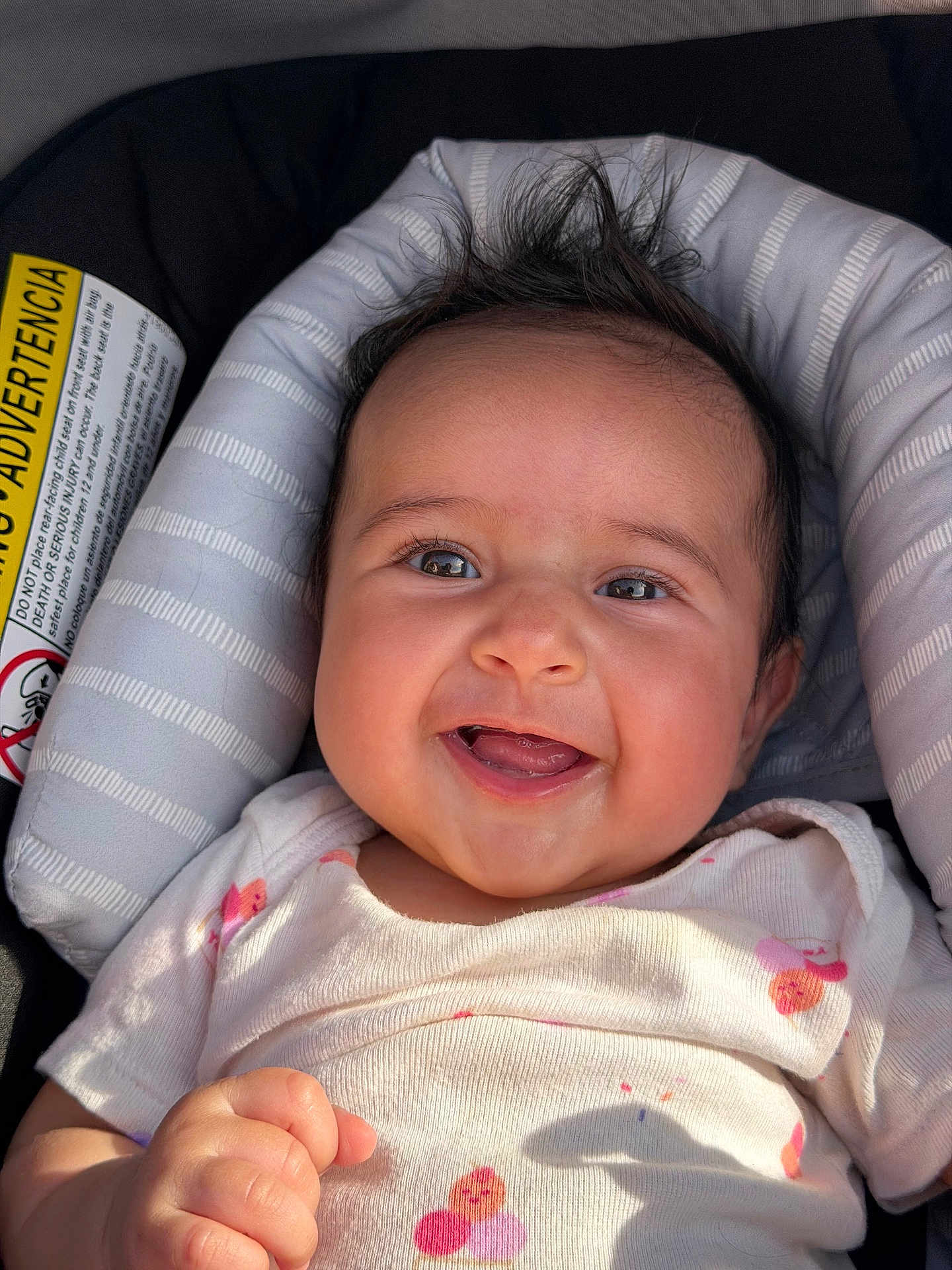 Berkeh is registered to the contest to win money with this photo: baby, infant, smiling, car_seat, onesie, hair, face, eyes, mouth, hand, closeup, portrait, cushion, seat, sunlight, shadow, label, sticker, happy, rosy_cheeks