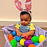 baby, child, bunny_ears, denim_overalls, yellow_shirt, basket, colorful_eggs, plastic_eggs, indoor, carpet, cute, smiling, playful, holiday, easter, toy, person, portrait, curly_hair, happy
