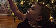Nova joined the competition — help win amazing prizes! baby, toddler, child, christmas_tree, ornament, tree_lights, holiday, dress, pearls, reaching, profile, sitting, carpet, curtain, interior, wood_floor, festive, decoration, soft_lighting, portrait