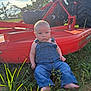 Camden is registered to the contest to win money with this photo: baby, denim_overalls, barefoot, grass, farm_equipment, red_machine, outdoor, sunlight, child, portrait, nature, greenery, serious_expression, grass_field, young_child, summer, rural, infant, sitting, daylight
