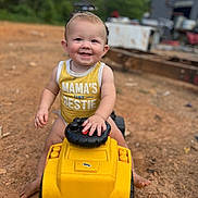 Easton is registered to the contest to win money with this photo: toddler, child, smiling, yellow_clothing, toy_vehicle, outdoor, dirt, happy, cute, person, summer, play, barefoot, tank_top, baby, nature, greenery, daylight, fun, portrait