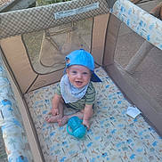 River joined the competition — help win amazing prizes! baby, bib, blue_cap, child, clothing, cute, face, grass, happy, headwear, infant, mesh, outdoor, pattern, person, playpen, sippy_cup, sitting, smiling, toy
