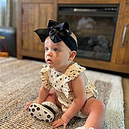 Celeste joined the competition — help win amazing prizes! baby, bow, carpet, child, clothing, curious, cute, fireplace, floor, footwear, headband, heart_pattern, indoor, infant, interior, portrait, romper, sitting, sneakers, wooden_cabinet