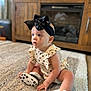 baby, bow, carpet, child, clothing, curious, cute, fireplace, floor, footwear, headband, heart_pattern, indoor, infant, interior, portrait, romper, sitting, sneakers, wooden_cabinet