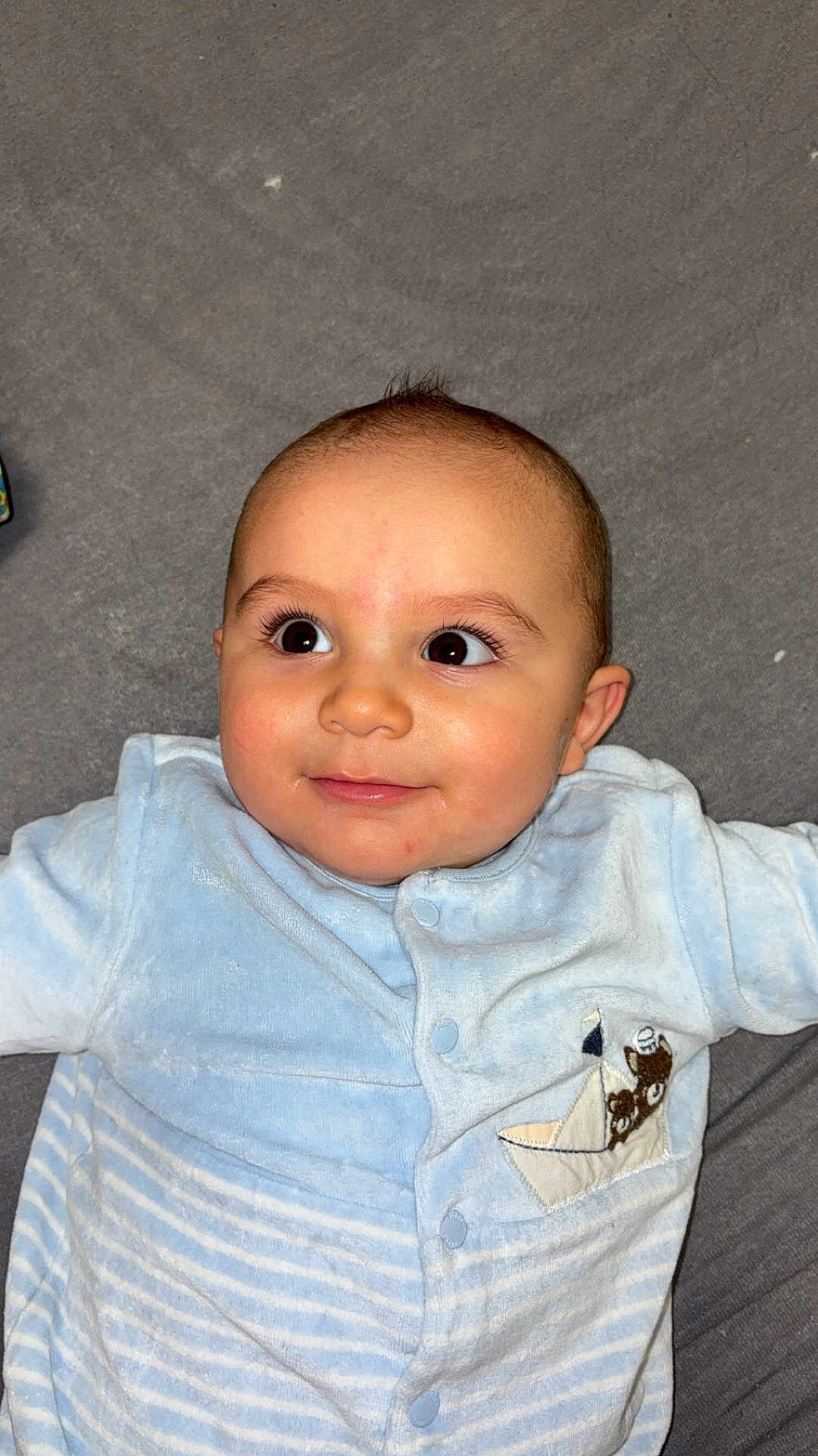 Fayver participe au concours pour gagner de l'argent avec cette photo : baby, infant, child, blue_clothing, onesie, teddy_bear_patch, boat_patch, smile, face, eyes, lying_down, soft_surface, cute, young_child, portrait, indoors, skin, head, expression, baby_garment