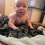 Waylon joined the competition — help win amazing prizes! baby, infant, blanket, floor, indoor, person, face, head, eyes, mouth, skin, storage_box, door, wood_floor, curious, child, young, crawling, cozy, home