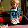 child, toddler, curly_hair, denim_jacket, dress, unicorn_pattern, restaurant, bench, sunlight, shadow, window, table, pink_table, closed_eyes, cute, indoor, daylight, casual_clothing, happy, portrait