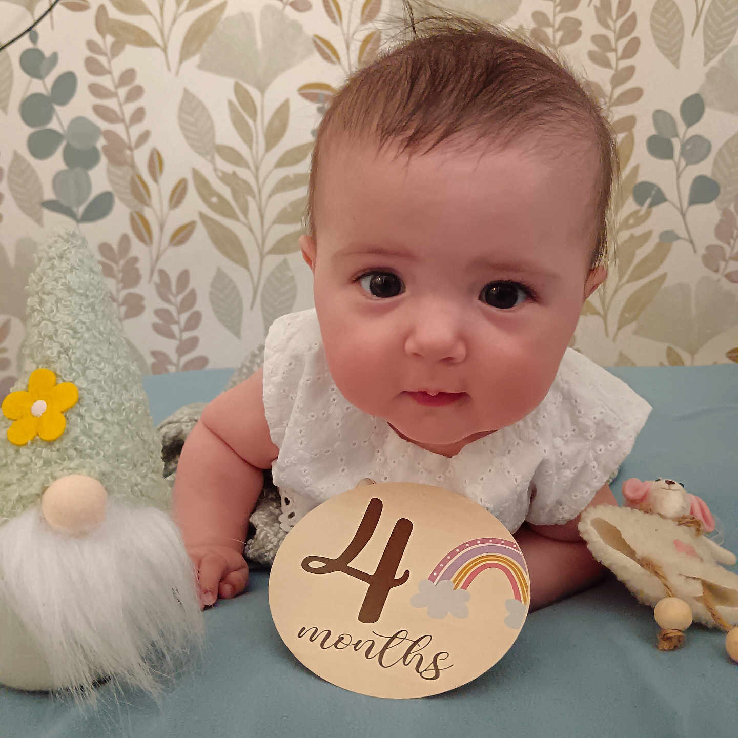Ava a rejoint le concours — aidez-le/la à gagner de superbes lots ! baby, infant, child, toy, gnome, soft_toy, blanket, blue_blanket, white_clothing, cute, portrait, face, eyes, smile, lying_down, indoor, floral_wallpaper, sign, rainbow, months