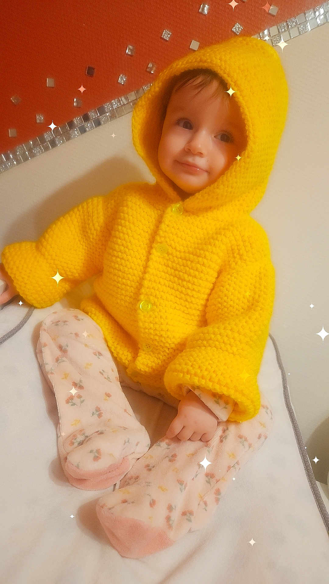 éva participe au concours pour gagner de l'argent avec cette photo : baby, child, yellow_hoodie, knitted_clothing, pajamas, floral_pattern, sitting, indoors, soft_surface, sparkles, cute, portrait, warm_clothing, infant, smiling, cozy, face, hand, feet, comfort