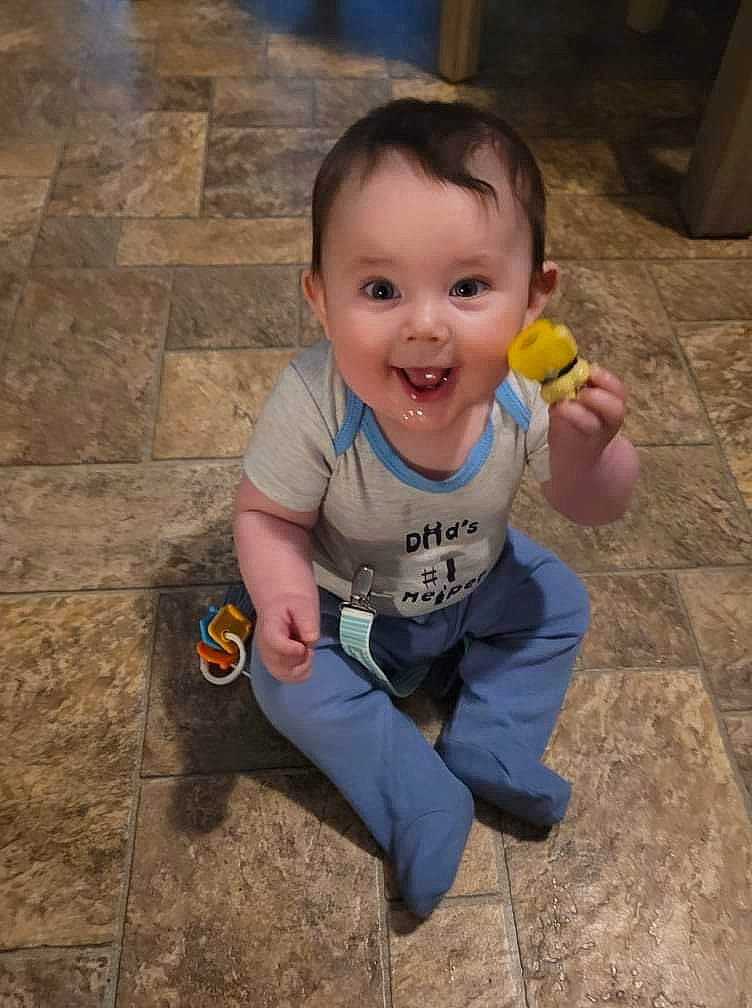 Jace is registered to the contest to win money with this photo: arm, baby, baby_toddler_clothing, cheek, cool, face, finger, floor, flooring, grass, hand, happy, joy, mouth, nose, person, sitting, smile, t_shirt, thumb