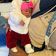 Aliya participe au concours pour gagner de l'argent avec cette photo : baby, sleeping, pink_headband, white_jacket, red_pants, white_booties, adult_hand, cozy_clothing, indoor, close_up, person, holding, warm, cute, newborn, soft_texture, casual, portrait, resting, infant