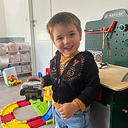 Gabriel participe au concours pour gagner de l'argent avec cette photo : child, toy_car, indoor, smiling, playroom, toy_workbench, colorful, jeans, hoodie, floor, plastic_toys, storage_bins, door, person, young_child, happy, playing, furniture, casual_clothing, blue_eyes