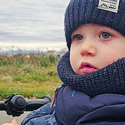 Gabriel participe au concours pour gagner de l'argent avec cette photo : toddler, child, hat, scarf, jacket, outdoor, winter_clothing, blue_eyes, face, portrait, cold_weather, nature, grass, cloudy_sky, closeup, person, young_child, expression, warm_clothing, seasonal