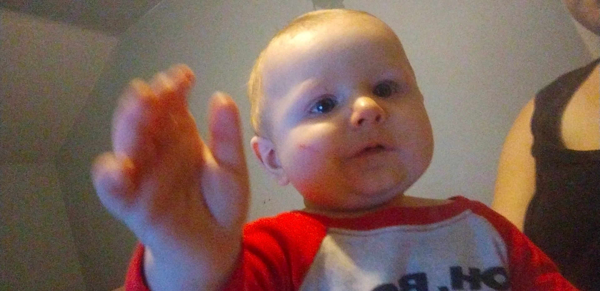 Jerimiah joined the competition — help win amazing prizes! baby, child, hand, face, curious, red_shirt, white_shirt, indoor, person, portrait, expression, skin, young_child, closeup, reaching, casual_clothing, adult_partial, background, room, photography