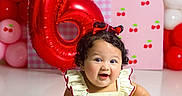 Paulina joined the competition — help win amazing prizes! baby, balloons, birthday, bow, celebration, cherries, child, curly_hair, dress, floor, happy, indoor, infant, number_six, party, portrait, red_balloon, sitting, smiling, studio