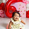 baby, balloons, birthday, bow, celebration, cherries, child, curly_hair, dress, floor, happy, indoor, infant, number_six, party, portrait, red_balloon, sitting, smiling, studio