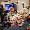 Lulu is registered to the contest to win money with this photo: bowl, candle, carpet, casual_clothing, countertop, cross, curtains, decor, dog, furniture, holding, indoor, pajamas, plant, shelf, shoes, sitting, smiling, television, woman