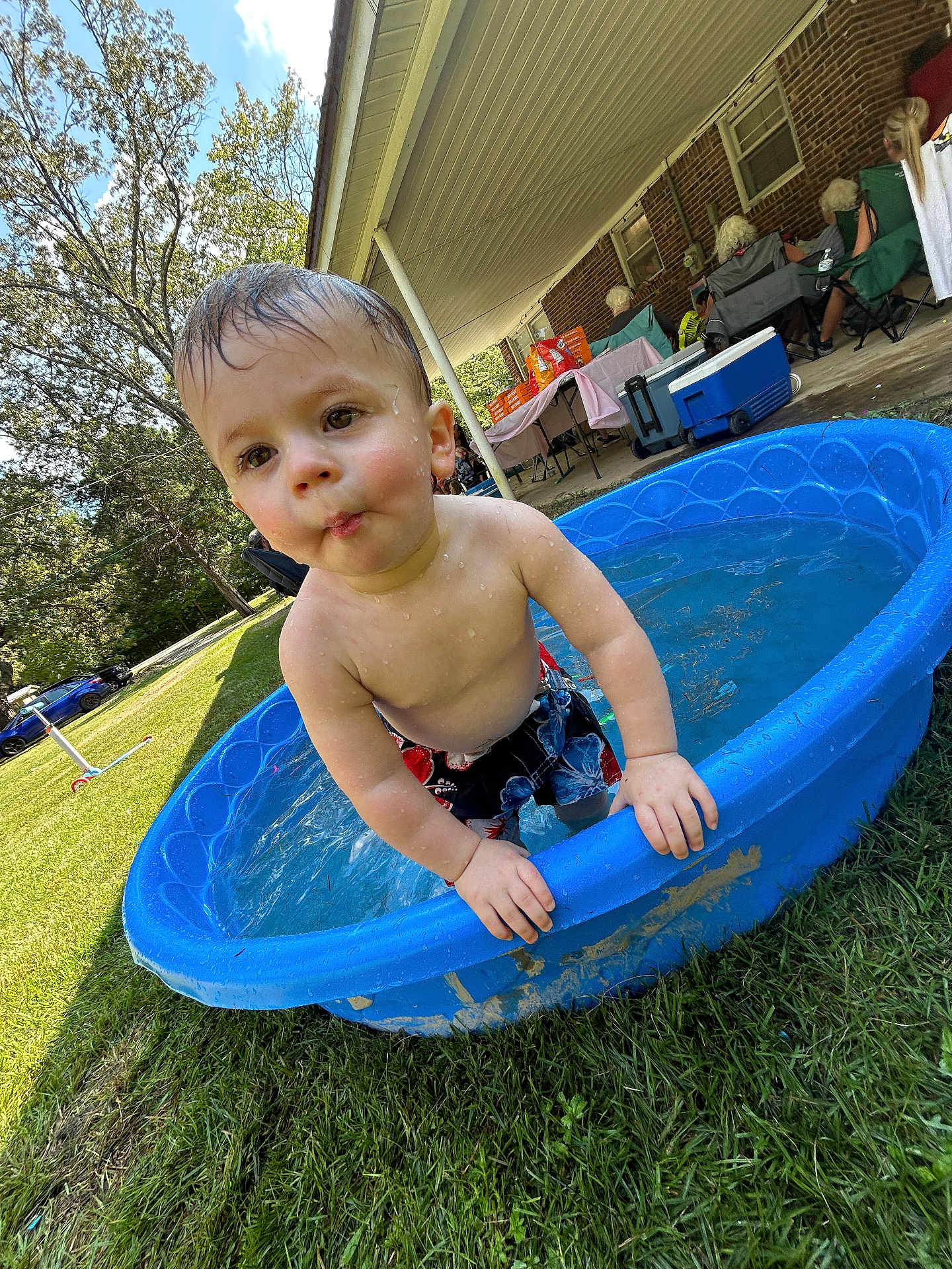 Axel is registered to the contest to win money with this photo: toddler, child, water, pool, blue_pool, grass, outdoor, summer, wet_hair, bare_chest, shorts, backyard, people, adults, chairs, cooler, table, trees, sunny, daytime