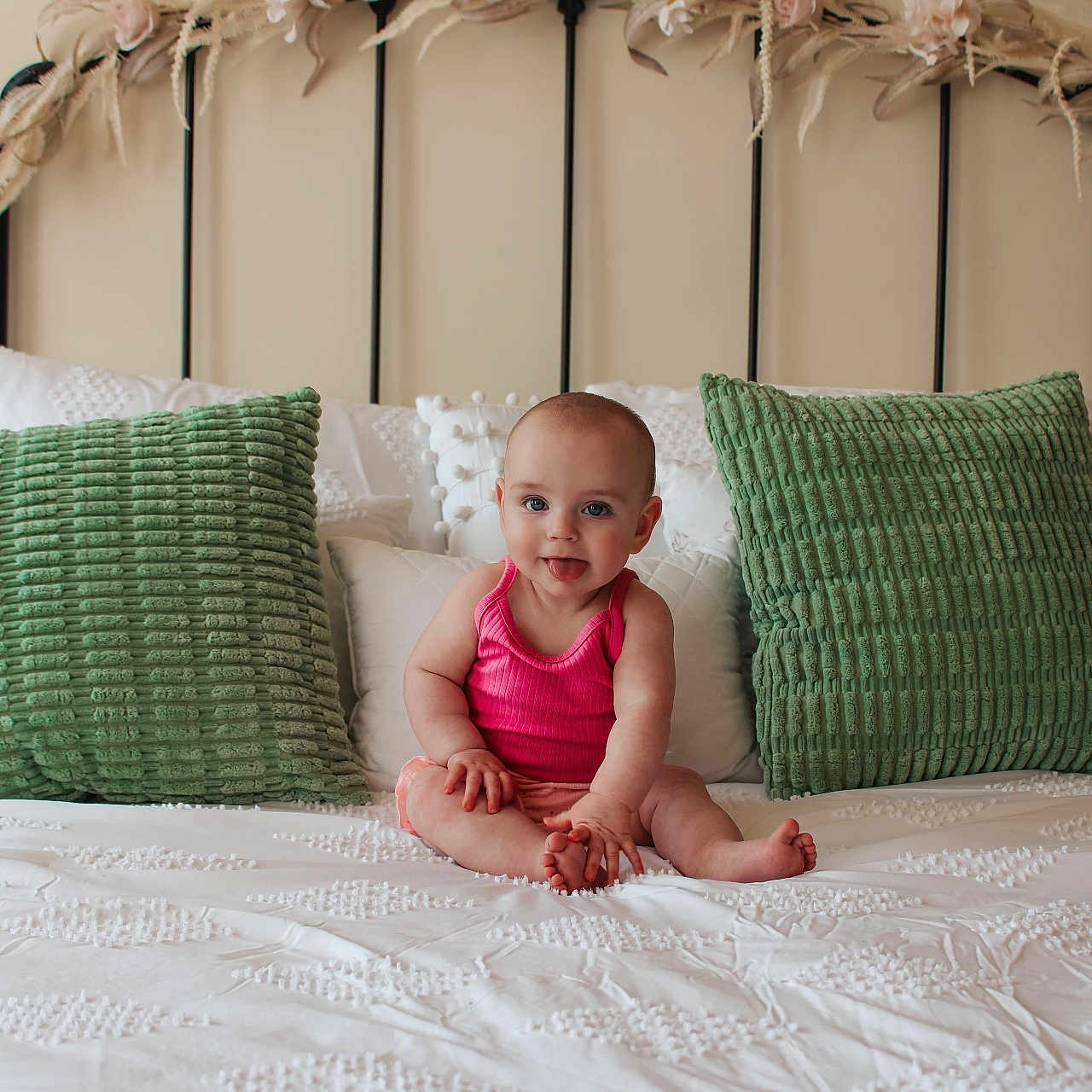 Olivianna joined the competition — help win amazing prizes! baby, bed, child, cute, dried_flowers, green_pillows, headboard, home_decor, indoor, infant, person, pillows, pink_clothing, portrait, sitting, smiling, soft_lighting, texture, tongue_out, white_bedding