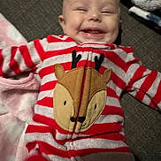 Izabella is registered to the contest to win money with this photo: apparel, baby, blanket, child, cozy, cute, expression, face, happy, indoors, infant, lying_down, onesie, portrait, red, reindeer_design, smiling, soft_texture, striped_clothing, white