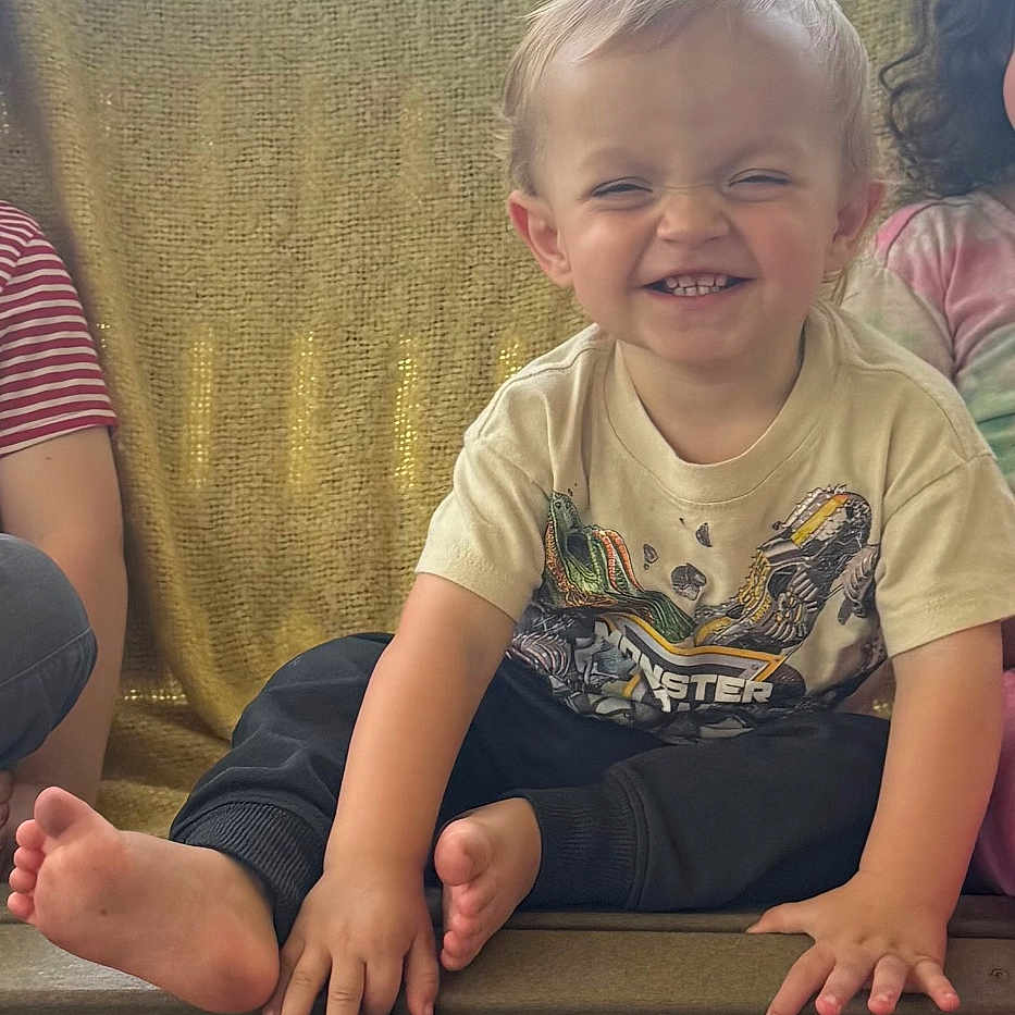 Bodie is registered to the contest to win money with this photo: toddler, child, smiling, barefoot, sitting, bench, yellow_blanket, graphic_tee, happy, outdoor, greenery, sky, portrait, casual, cute, people, candid, daylight, fun, young_child