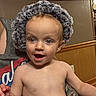 Bodie is registered to the contest to win money with this photo: toddler, child, hat, fluffy_hat, happy, smiling, indoor, person, face, skin, bare_chest, expression, adult_arm, tattoo, wood_paneling, wall, furniture, casual, portrait, cute