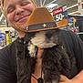 person, puppy, dog, cowboy_hat, black_and_white, fluffy, holding, store, indoor, smiling, happy, retail, price_tag, shelf, casual, young_adult, short_hair, hand, cute, pet