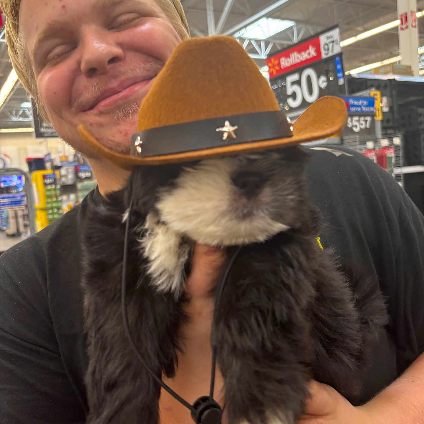 Rocky is registered to the contest to win money with this photo: black_and_white, casual, cowboy_hat, cute, dog, fluffy, hand, happy, holding, indoor, person, pet, price_tag, puppy, retail, shelf, short_hair, smiling, store, young_adult
