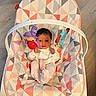 Valerie is registered to the contest to win money with this photo: baby, infant, child, bouncer, baby_seat, toy, rattle, hanging_toy, indoor, wooden_floor, portrait, lying_down, white_clothing, pink_pants, harness, geometric_pattern, colorful, face, newborn, home