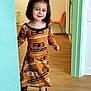 balenciaga, child, childhood, cute, doorway, dress, fashion, floor, girl, hair_bow, happy, indoor, interior, orange_chair, person, sandals, smile, standing, wood, young