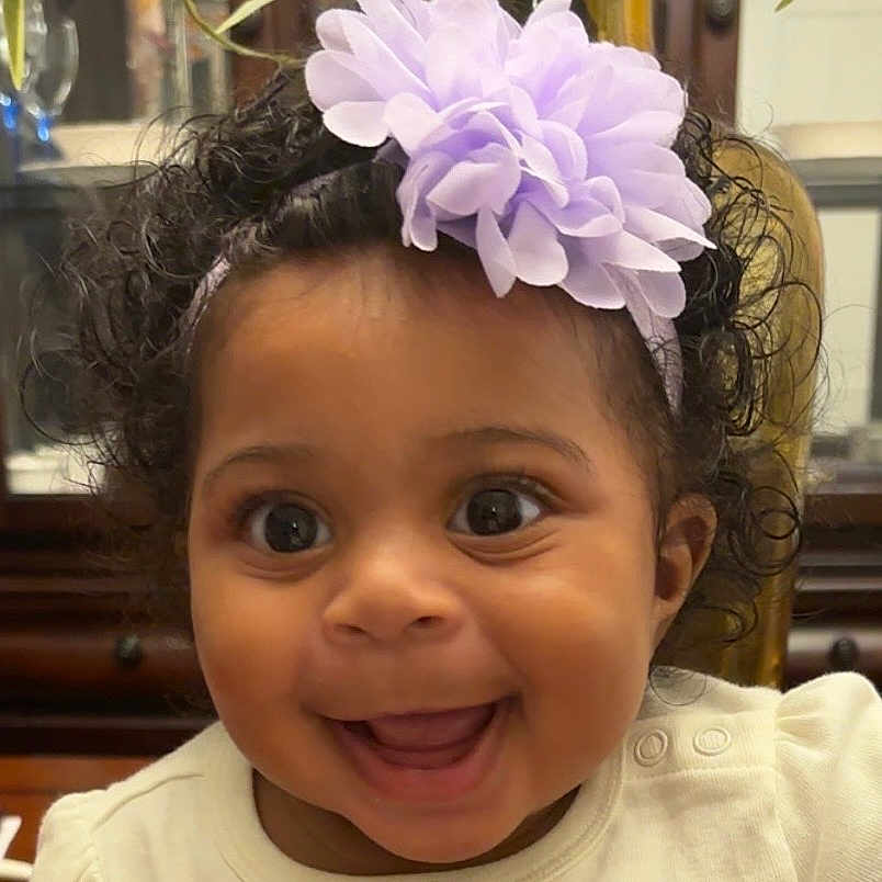 Haliey is registered to the contest to win money with this photo: adorable, apparel, baby, baby_girl, cheerful, child, closeup, curly_hair, cute, face, flower, happy, headband, indoors, infant, joy, person, portrait, smiling, white_clothing