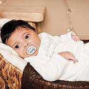 Djessim a rejoint le concours — aidez-le/la à gagner de superbes lots ! baby, big_eyes, binky, blanket, calm, cozy, cute, dark_hair, hand, indoor, infant, knitted_throw, lying_down, newborn, pacifier, portrait, soft_texture, white_clothing, wicker_basket, wooden_table