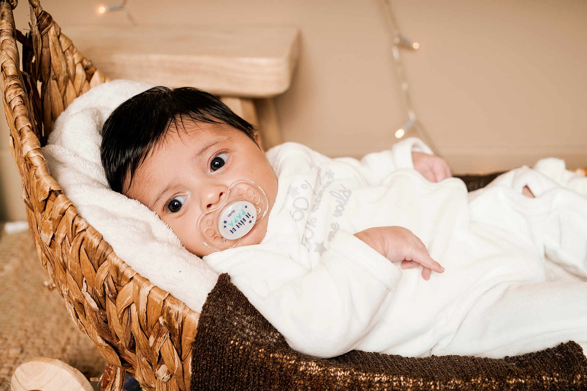 Djessim a rejoint le concours — aidez-le/la à gagner de superbes lots ! baby, big_eyes, binky, blanket, calm, cozy, cute, dark_hair, hand, indoor, infant, knitted_throw, lying_down, newborn, pacifier, portrait, soft_texture, white_clothing, wicker_basket, wooden_table
