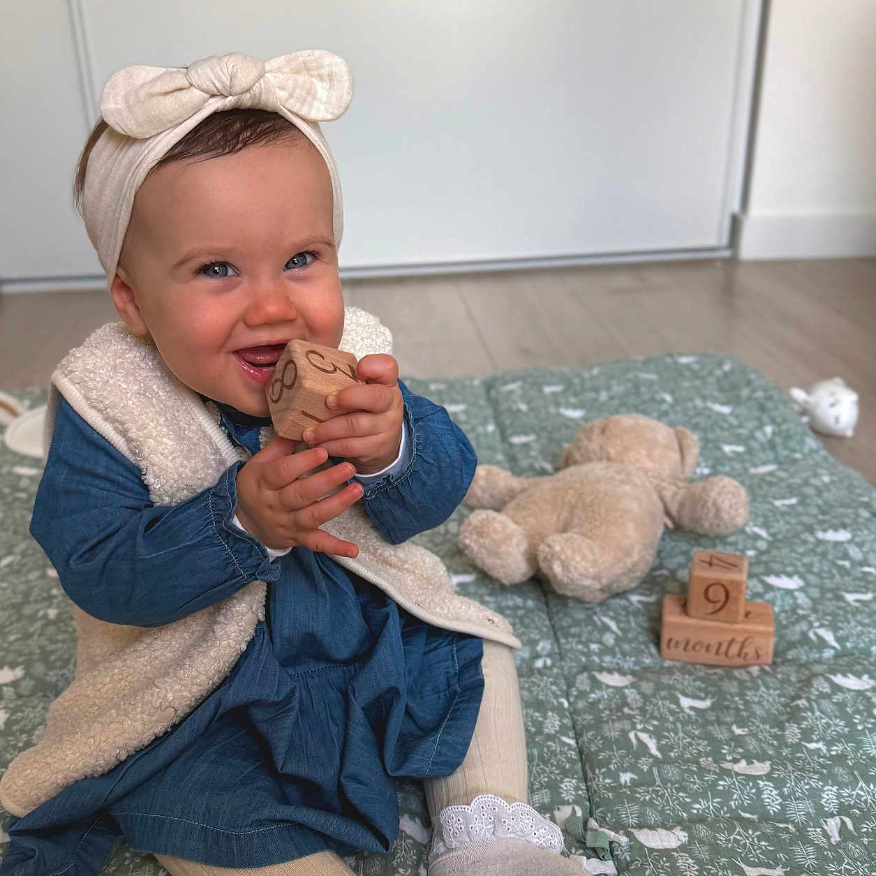Layana participe au concours pour gagner de l'argent avec cette photo : baby, blue_dress, child, cute, floor, girl, happy, headband, indoor, mat, patterned, playful, portrait, sitting, smiling, sock, teddy_bear, tights, toy, wooden_block