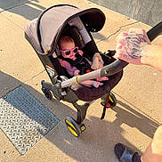 Oaklynn joined the competition — help win amazing prizes! baby, sunglasses, stroller, outdoor, sidewalk, sunlight, shadow, person, hand, tattoo, footwear, casual_clothing, infant, plastic, wheel, canopy, safety_harness, toy, concrete, urban
