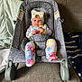 Oaklynn is registered to the contest to win money with this photo: baby, infant, headband, bow, tie_dye, footed_pajamas, baby_rocker, gray, couch, blanket, indoor, child, seated, curious_expression, soft_lighting, cozy, comfort, person, young_child, home