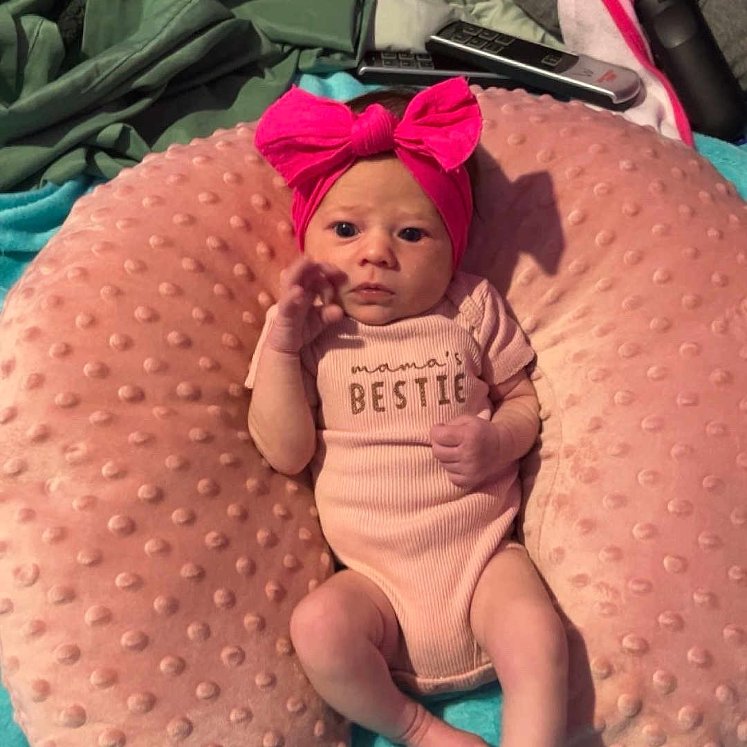 Oaklynn joined the competition — help win amazing prizes! baby, baby_girl, blanket, child, comfortable, cozy, curious, cute, headwear, indoor, infant, laying_down, newborn, onesie, pillow, pink_bow, portrait, remote_control, small_hands, soft_texture